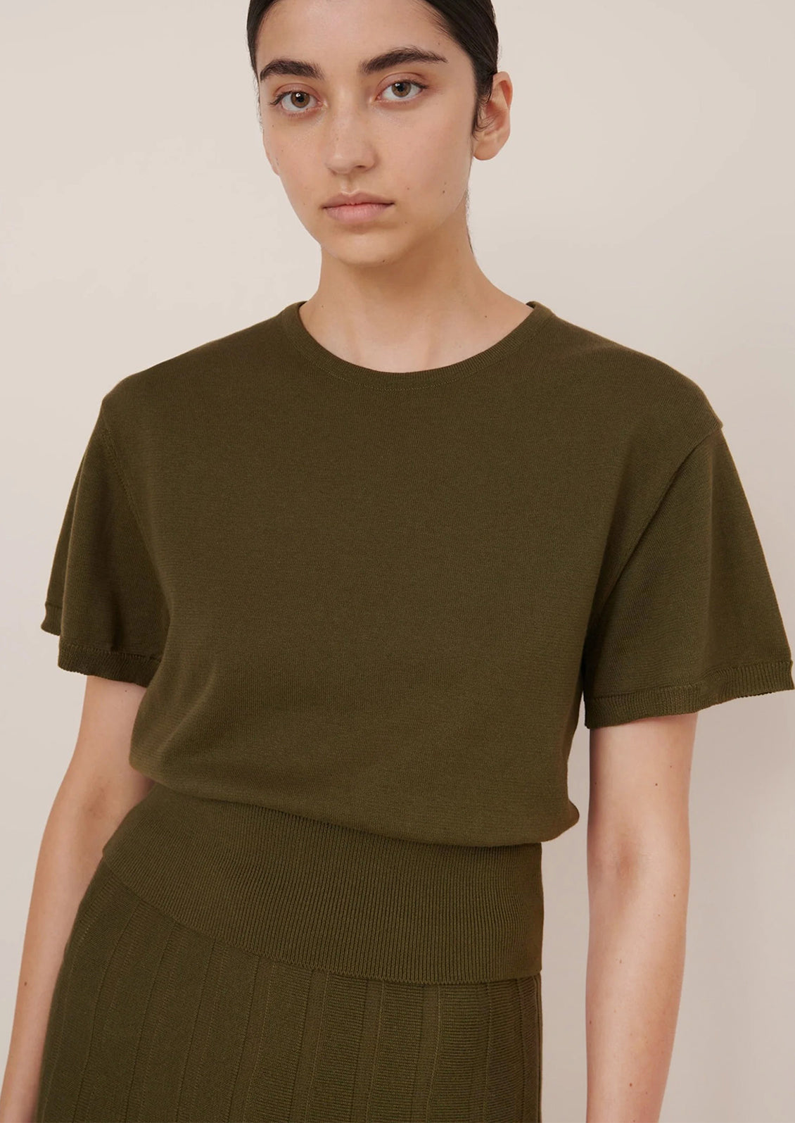 Person wearing an olive green t-shirt and skirt against a plain background