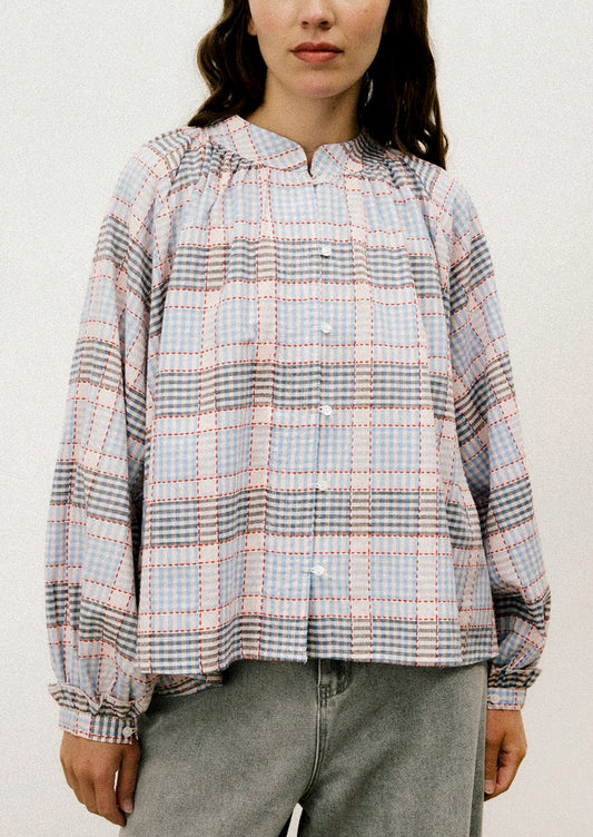 A person wearing a long sleeve blouse with blue and red plaid pattern.