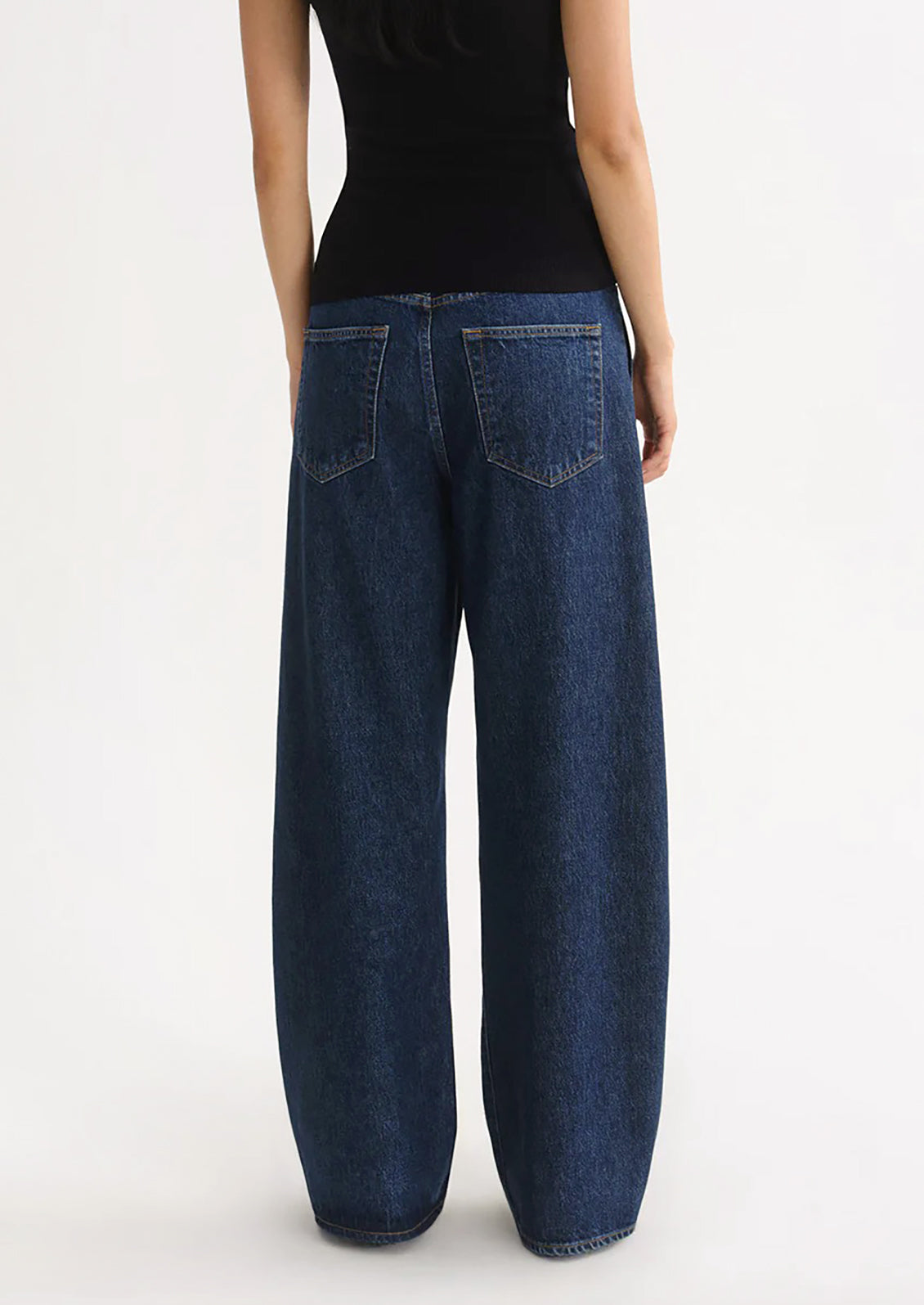 A person wearing a pair of dark denim jeans with pleated pocket front.