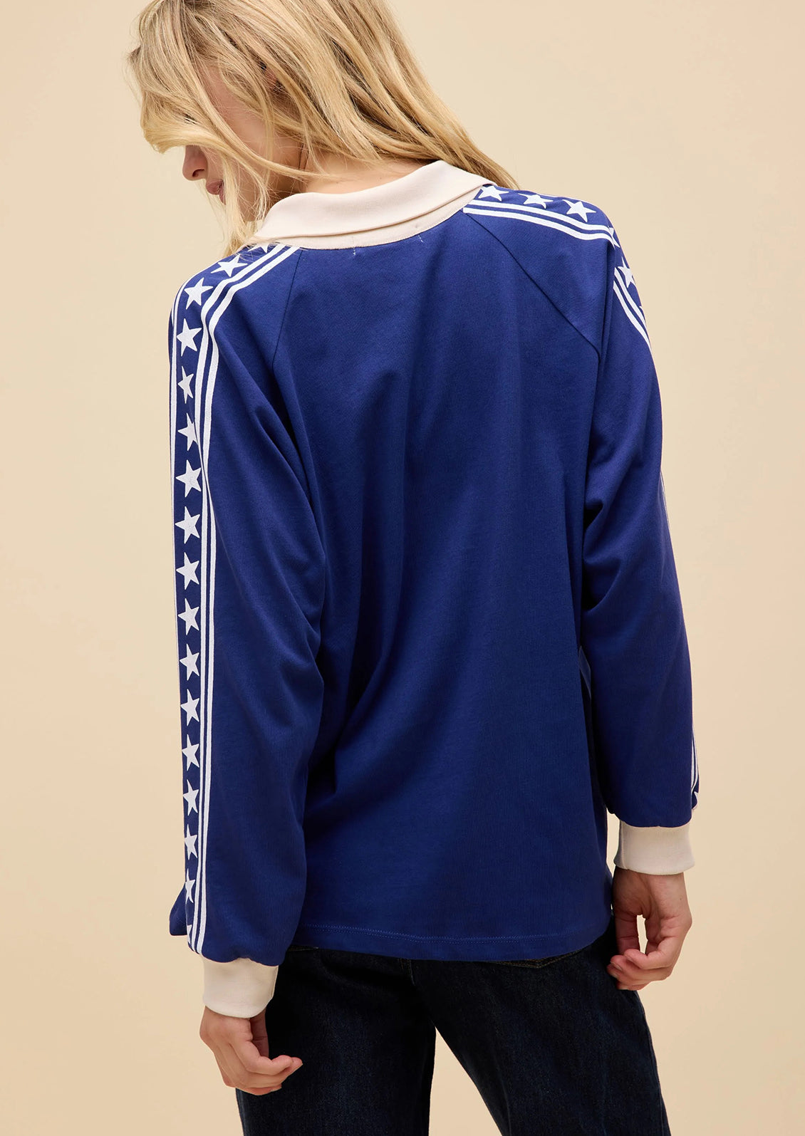Blue long-sleeve shirt with white star patterns on sleeves against a beige background