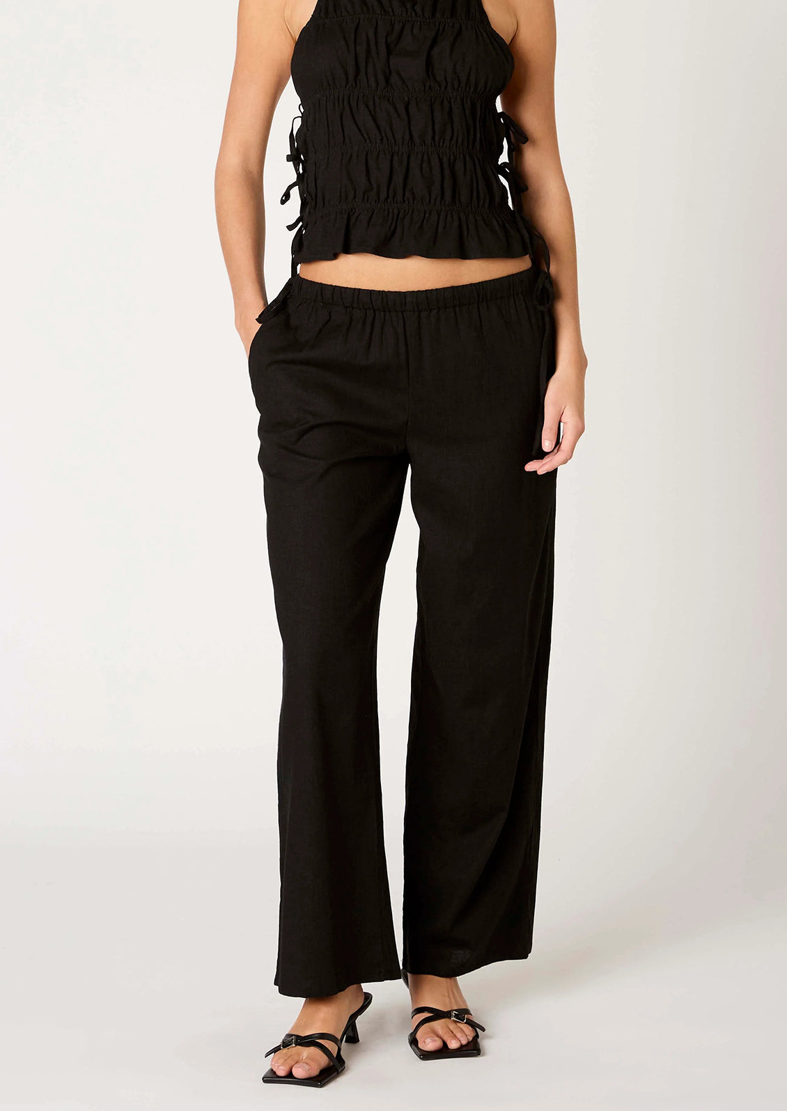 A person wearing a pair of relaxed black wide leg trousers with side tie detail at waist.