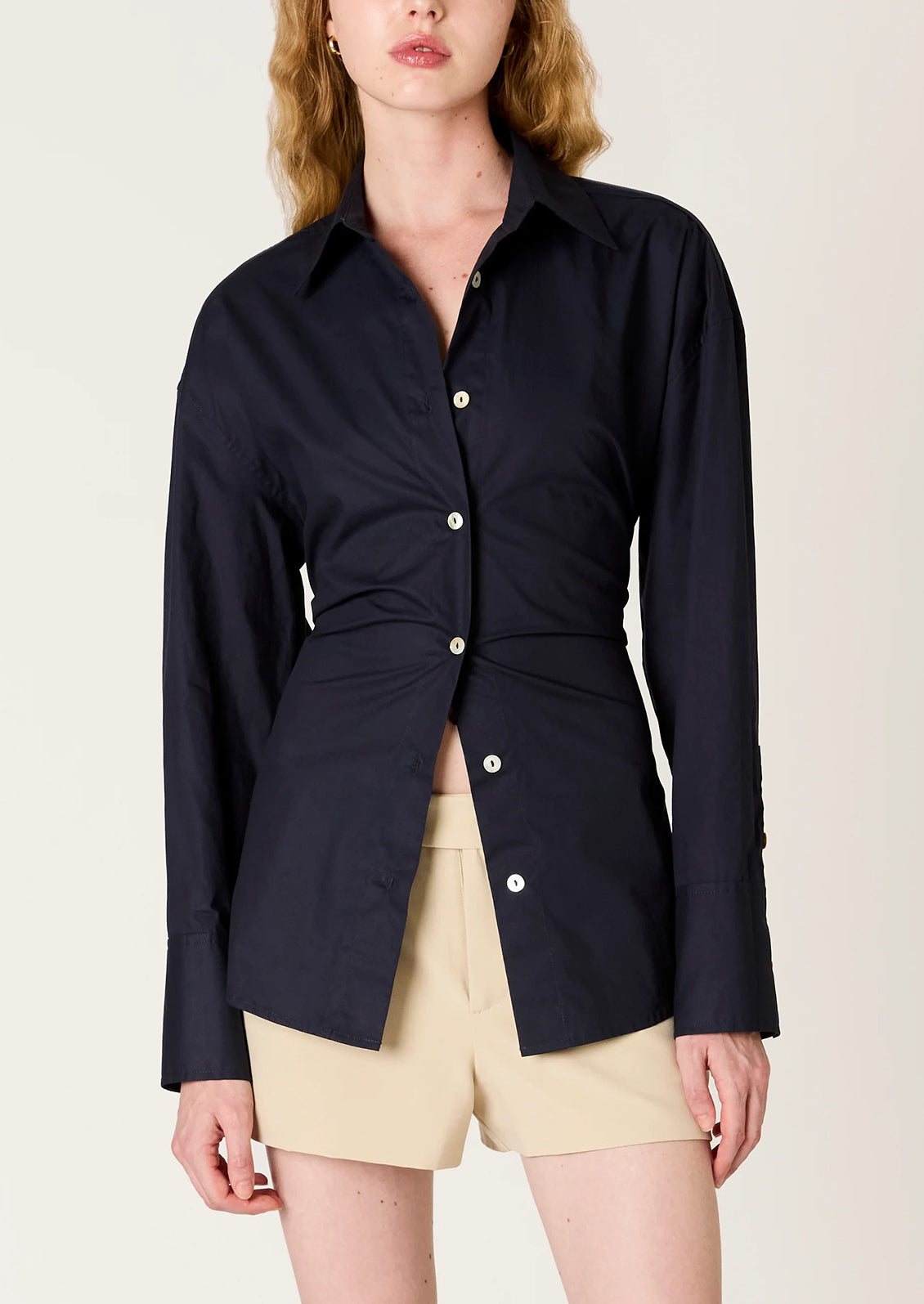 Woman wearing a navy blue shirt with a tie-waist design on a beige background