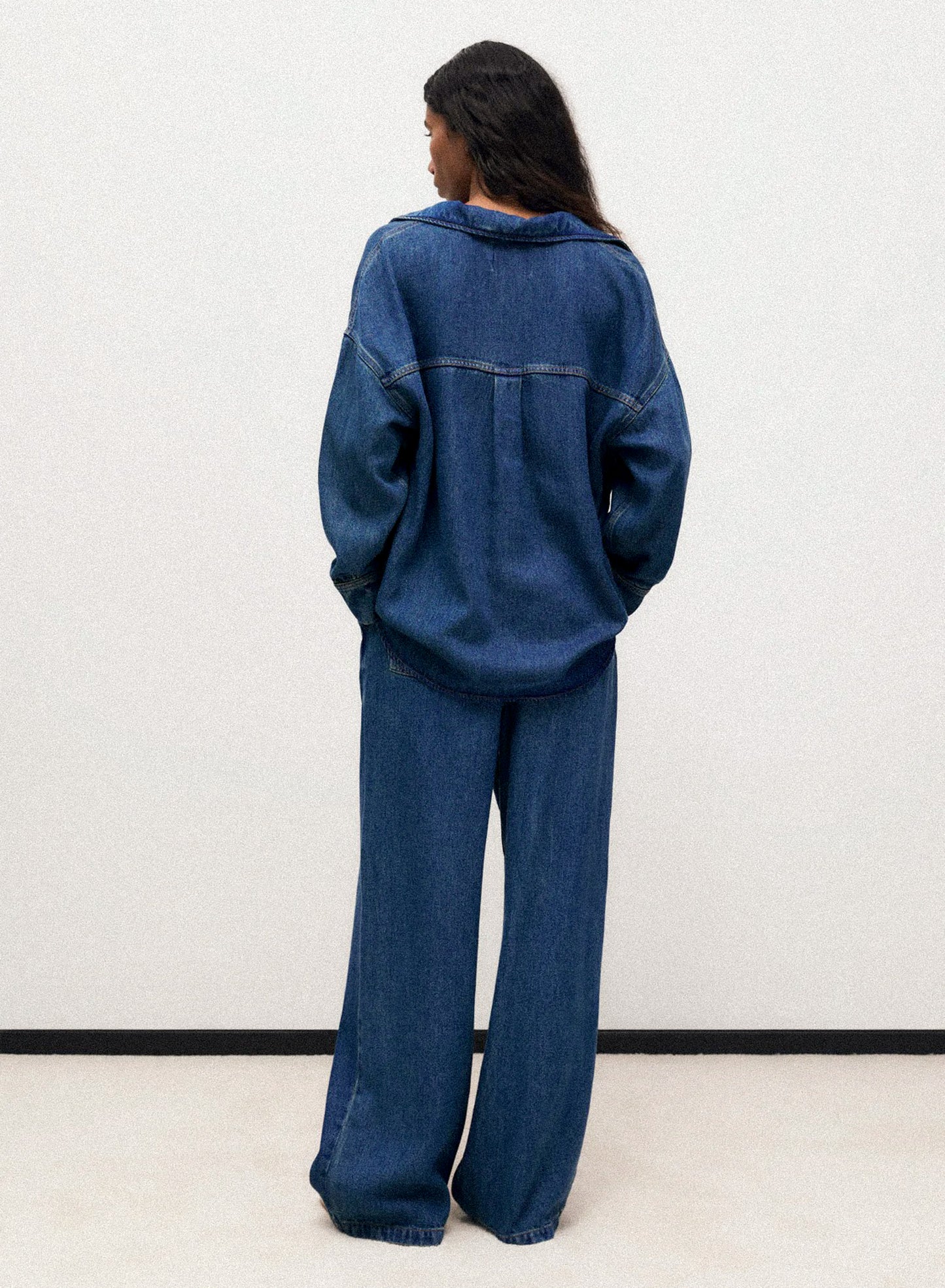 A woman wearing a pair of pleat front wide leg pants in blue denim.