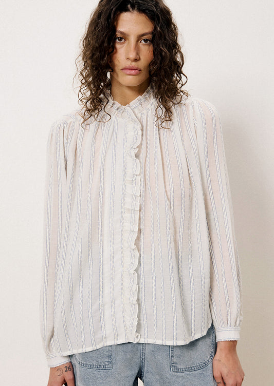 A woman wearing a long sleeve blouse with ruffle front placket and interwoven stripe detail throughout.