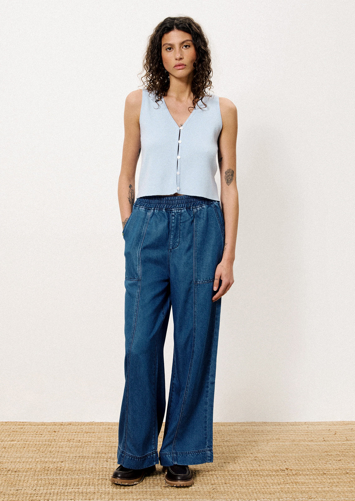 A person wearing a pair of relaxed denim pants with elasticized waistband.