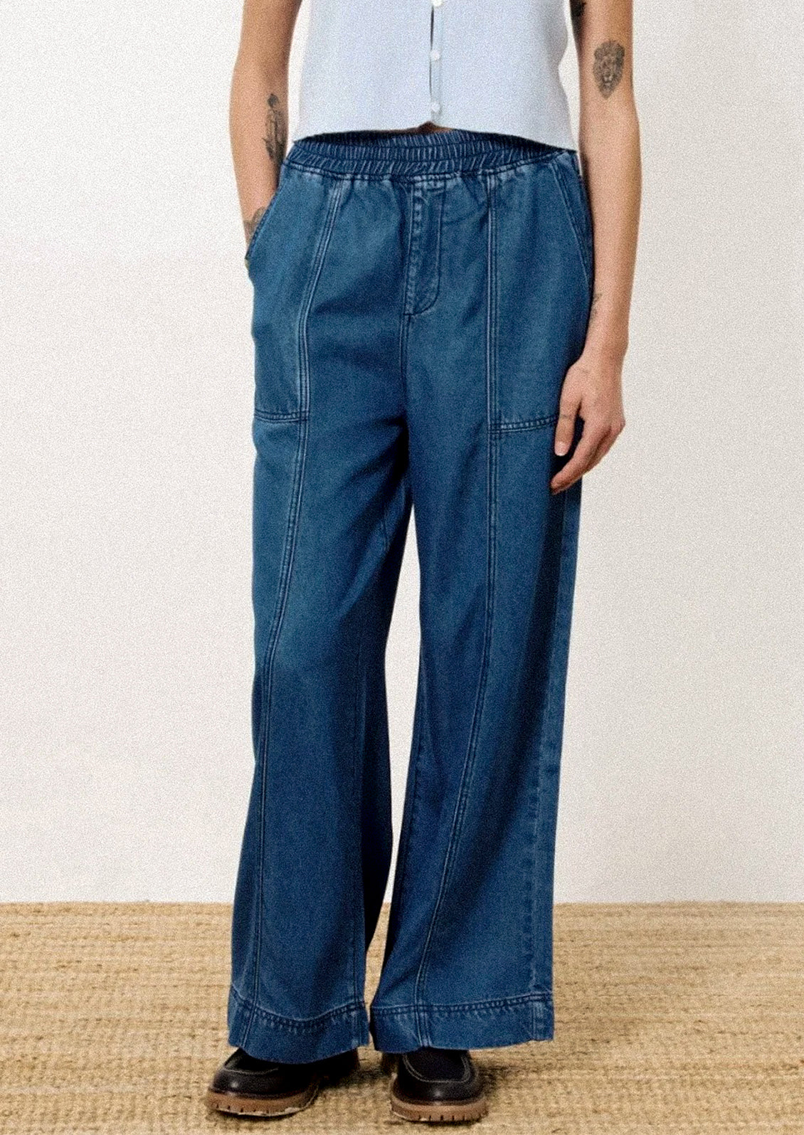 A person wearing a pair of relaxed denim pants with elasticized waistband.