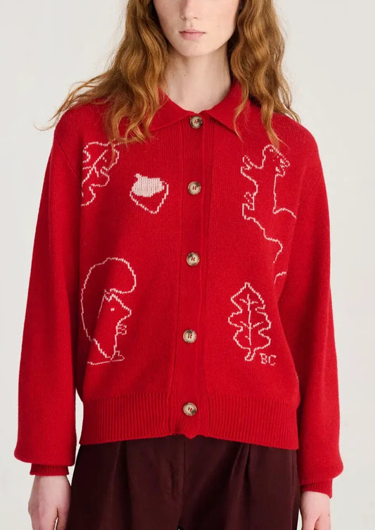 A red knit cardigan sweater with white knitted animal and leaf motifs, featuring gold buttons and a collar, worn by a model.