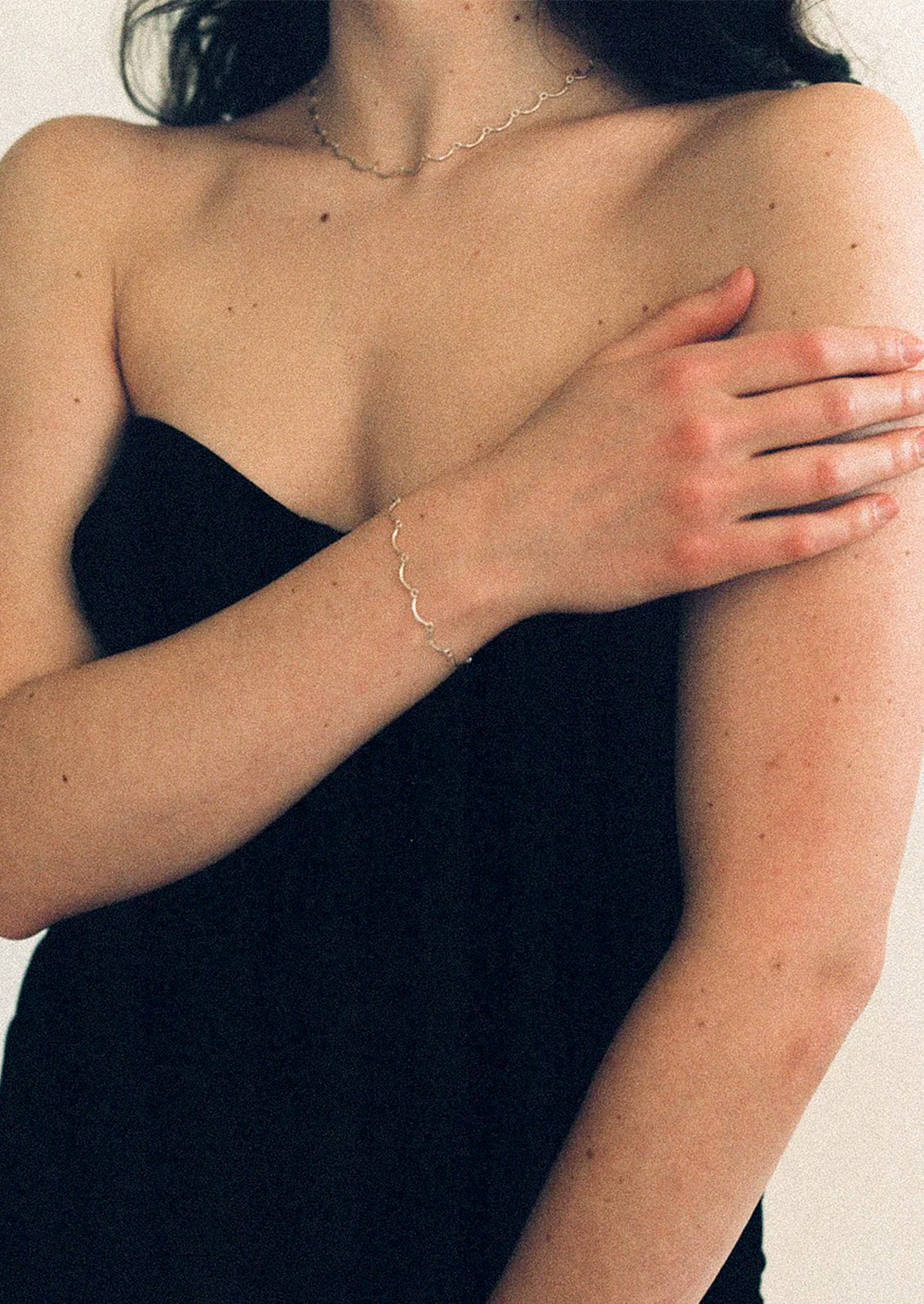 Person wearing a black strapless top with a gold bracelet on a neutral background