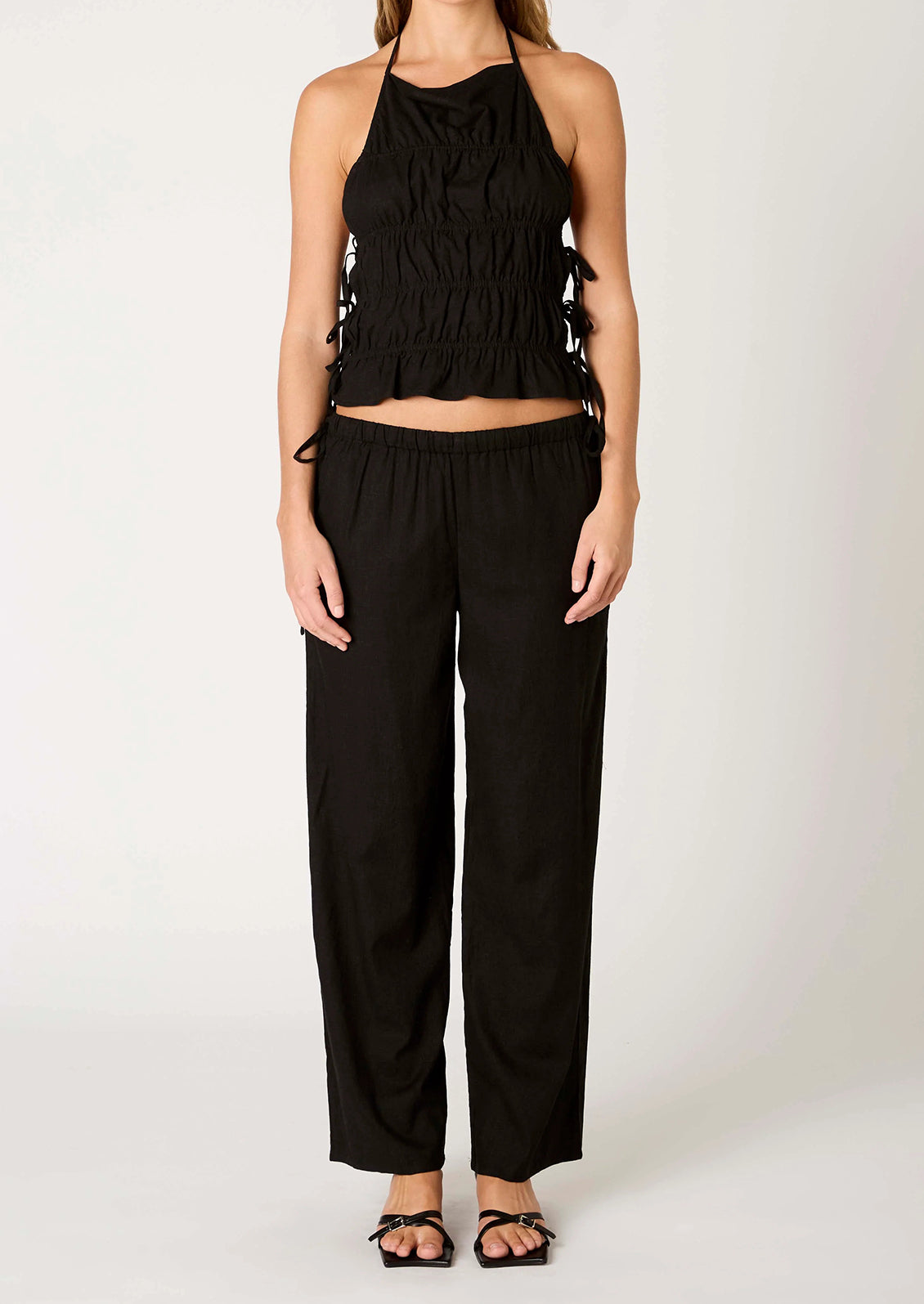 A person wearing a pair of relaxed black wide leg trousers with side tie detail at waist.