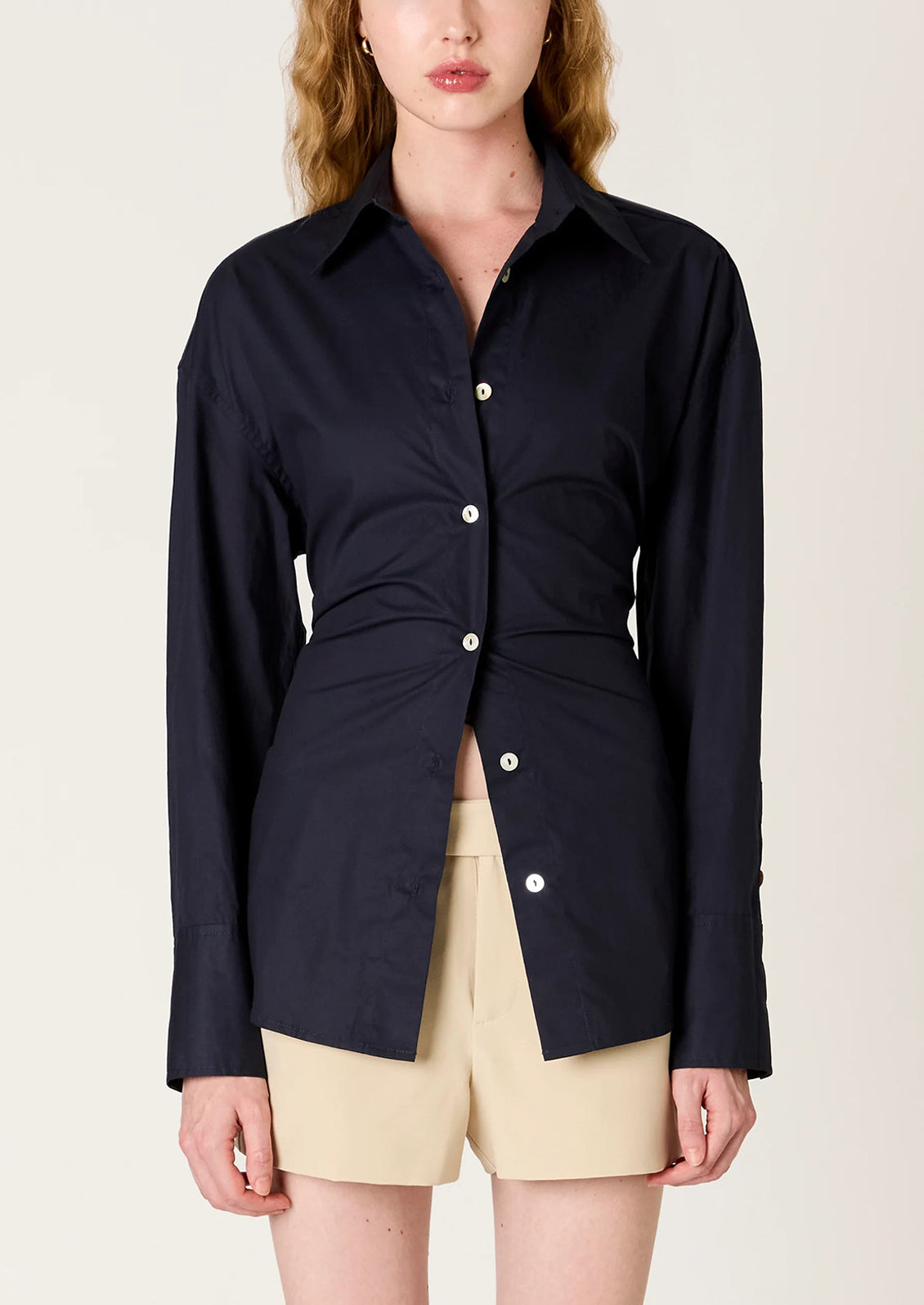 Person wearing a navy blue shirt with a tie-waist design on a beige background