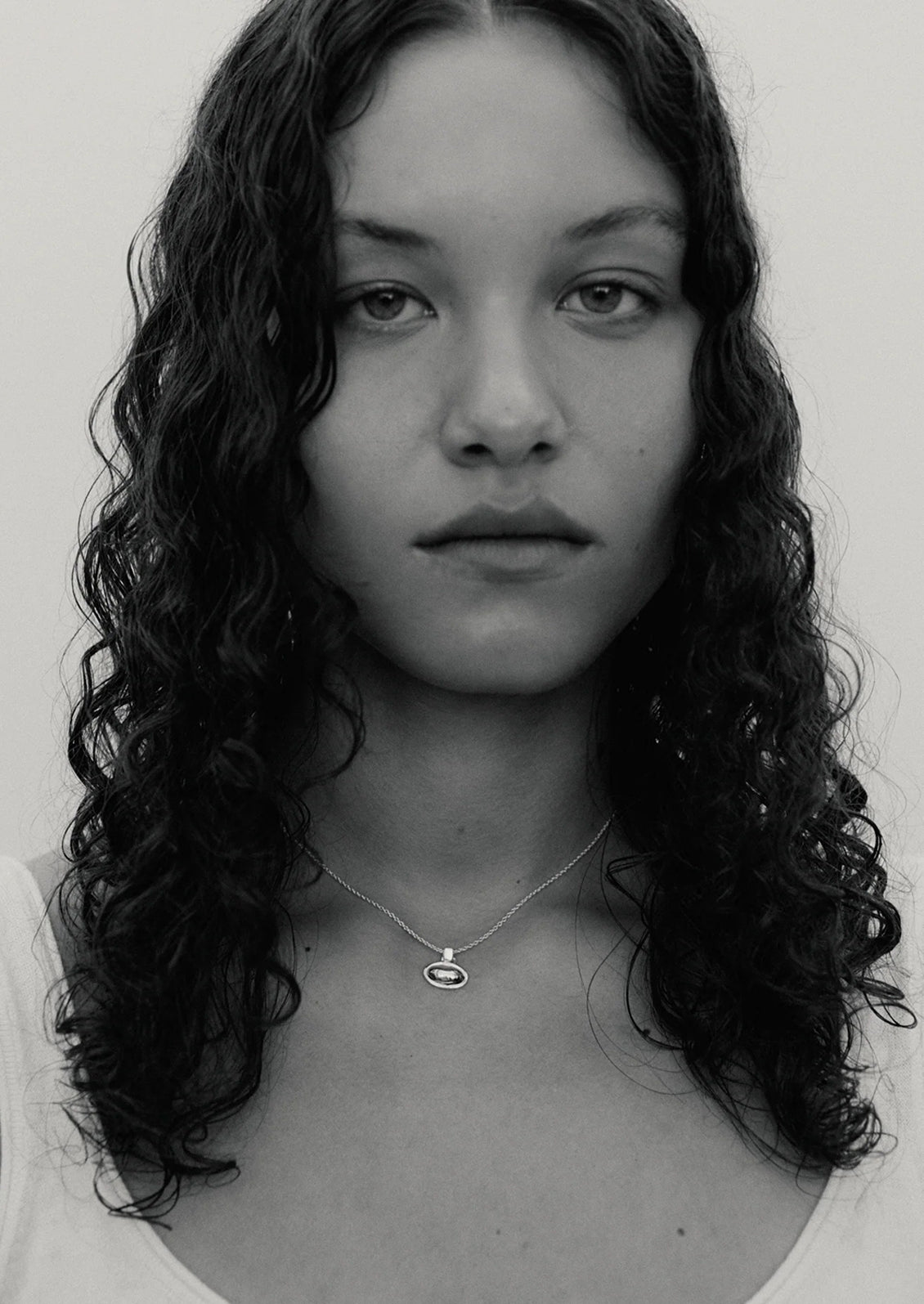 Black and white portrait of a person with wavy hair wearing a necklace.
