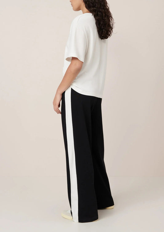 Person wearing a white top and black pants with a white stripe on a beige background