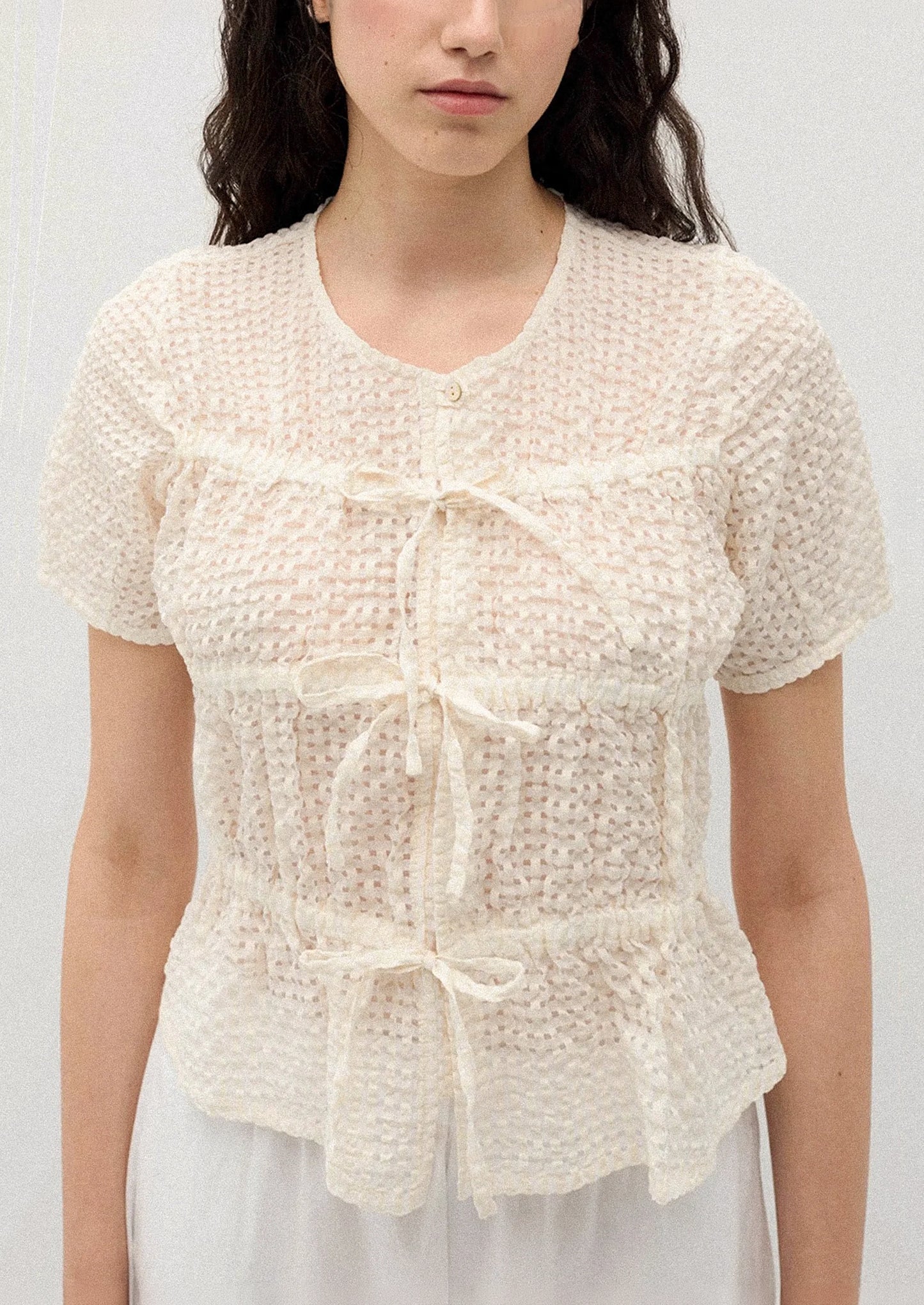 A person wearing a crinkled short sleeve top in cream.
