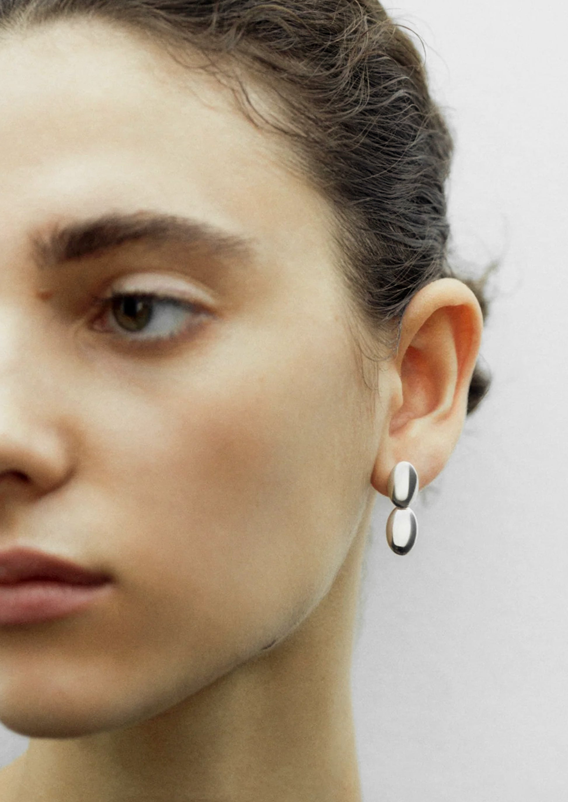 Close-up of a person wearing a unique earring on a plain background
