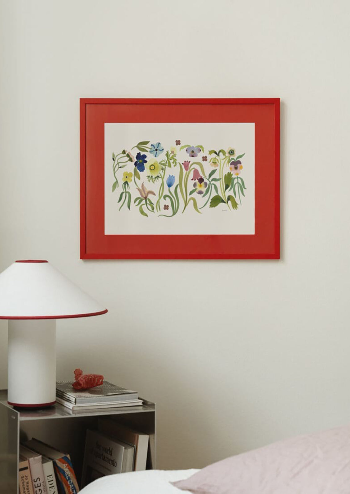 Framed floral artwork on a wall above a nightstand with a lamp and books.