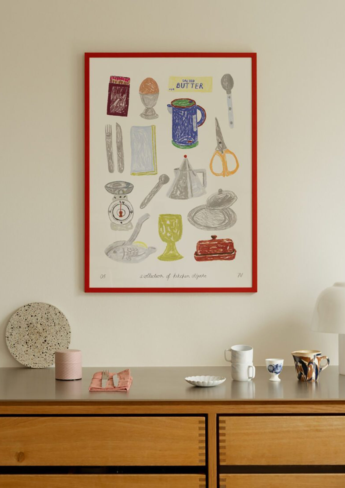 Framed kitchen-themed artwork on a wall above a wooden dresser with decorative items.