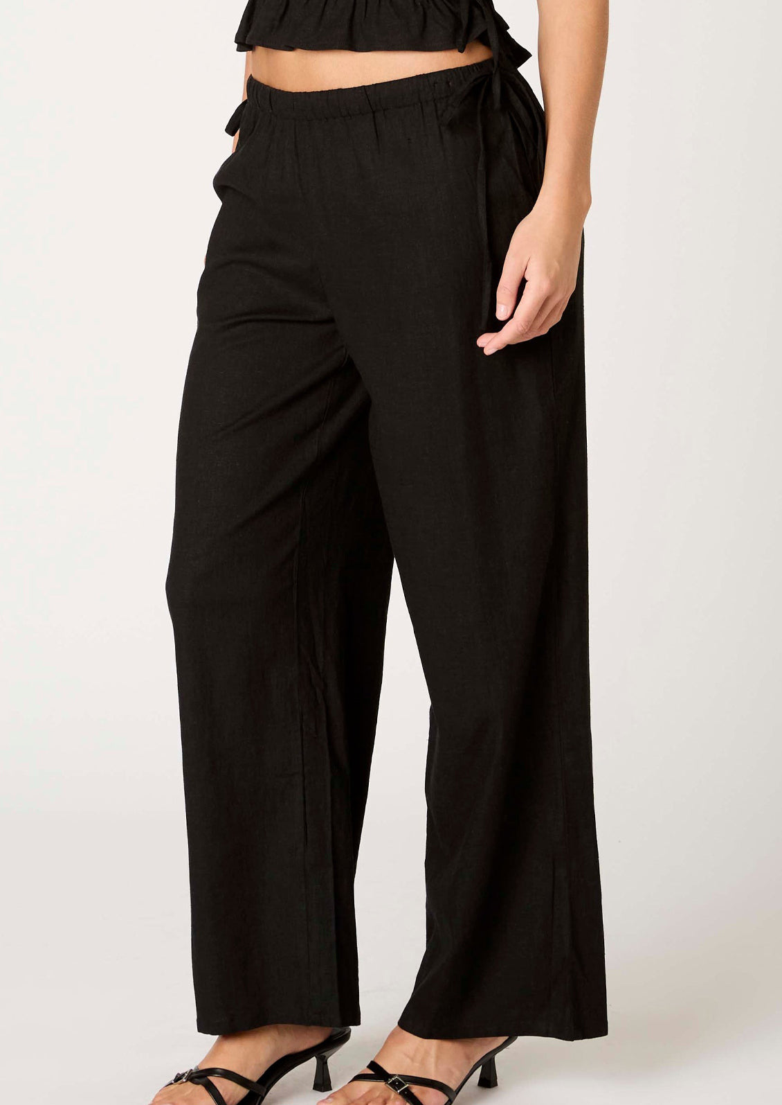 A person wearing a pair of relaxed black wide leg trousers with side tie detail at waist.