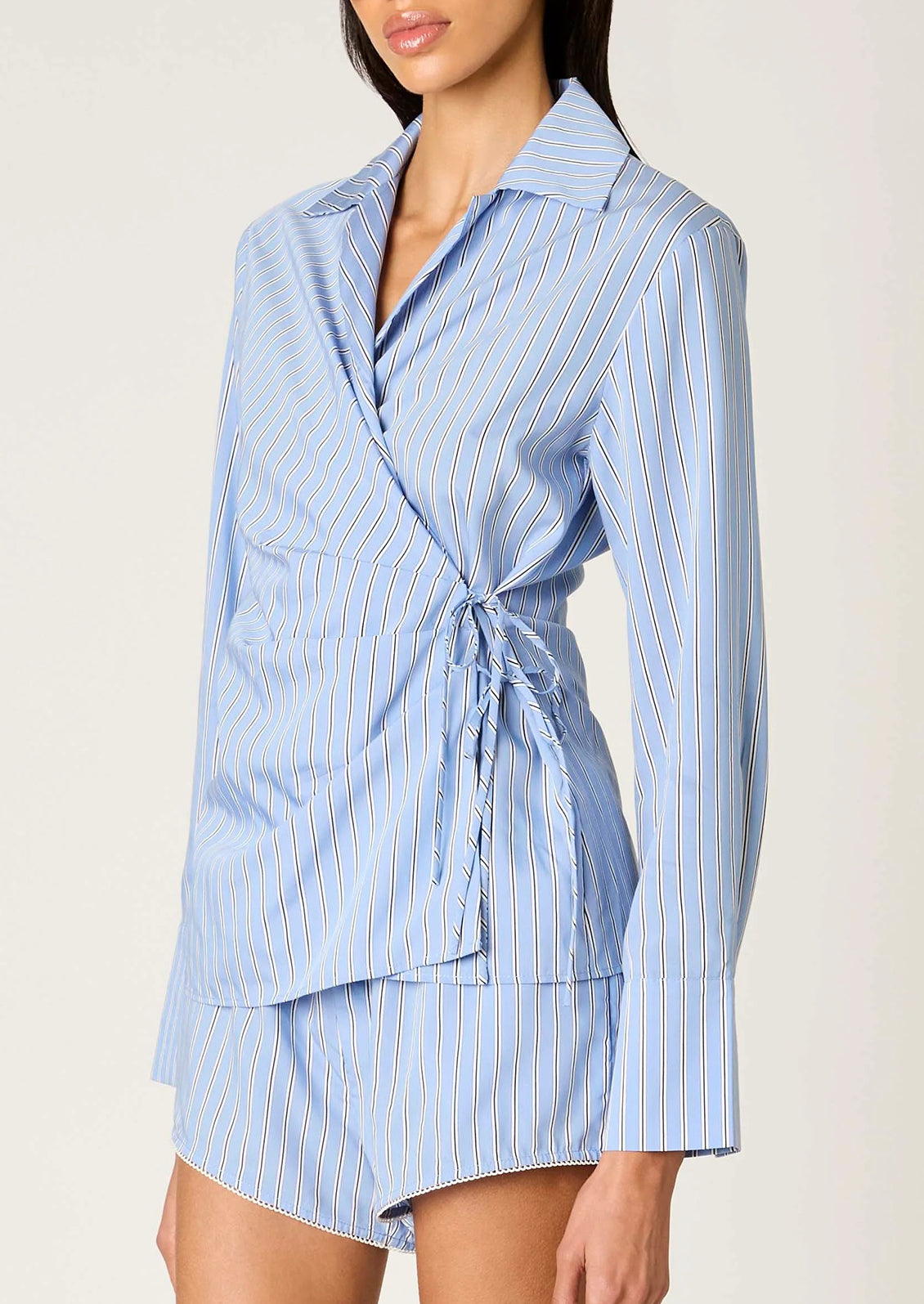 Woman wearing a blue striped shirt and shorts set on a plain background