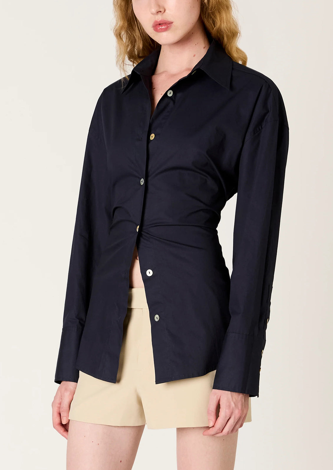 Person wearing a navy blue shirt with a tie-waist design on a beige background