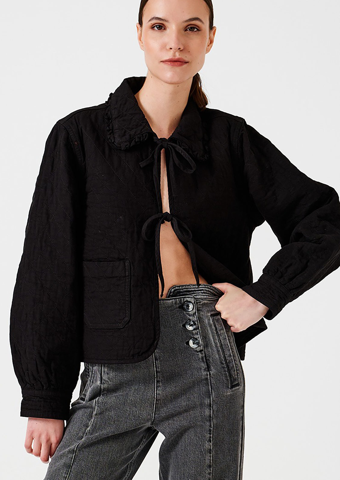 Woman wearing a black cropped jacket with a tie detail on a white background