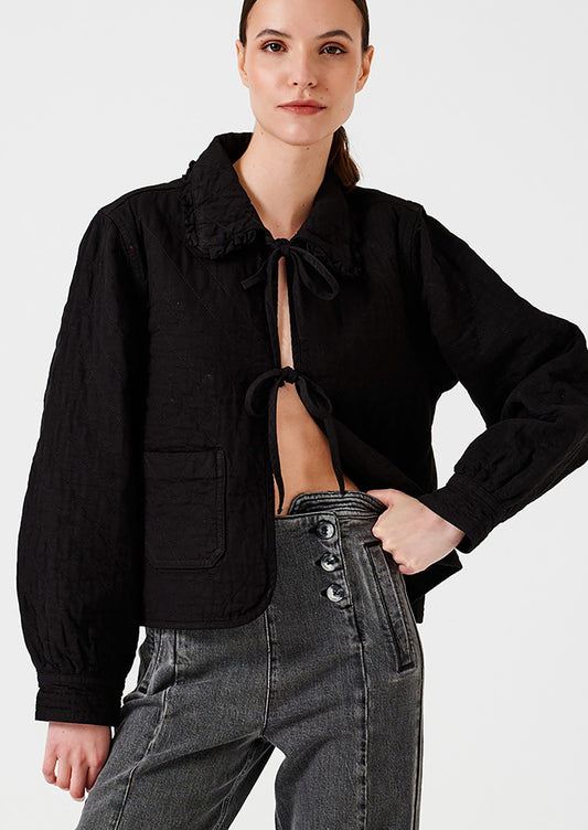 Woman wearing a black cropped jacket with a tie detail on a white background