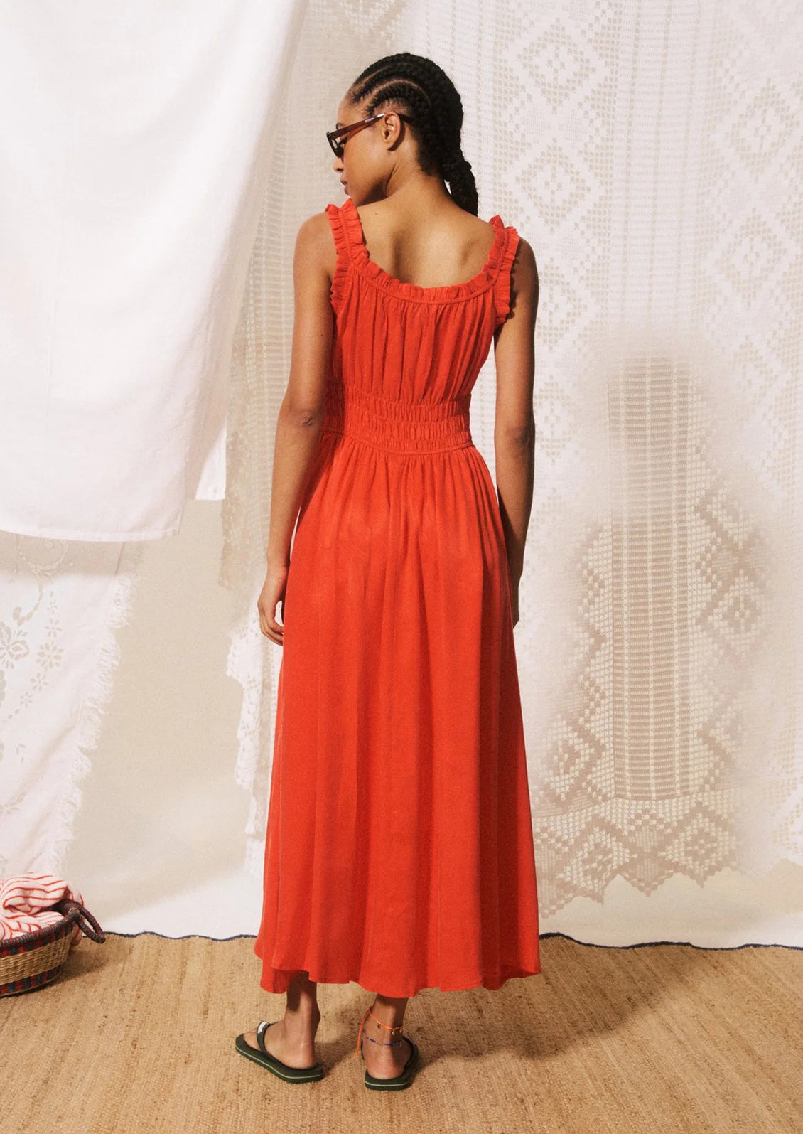 A woman modeling a bright orange-red midi dress with ruffled straps, a gathered bodice, and a flowing skirt.