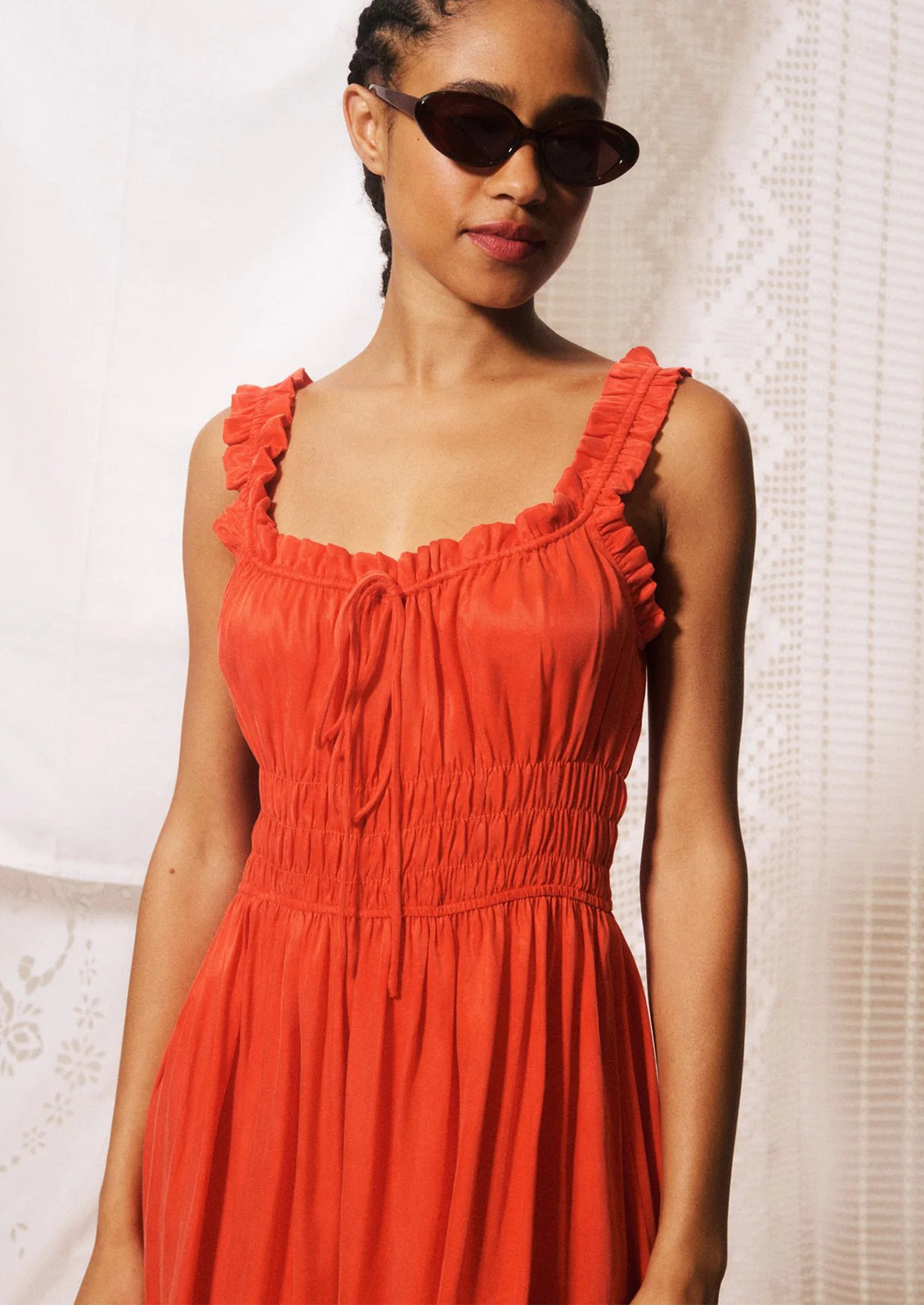 A woman modeling a bright orange-red midi dress with ruffled straps, a gathered bodice, and a flowing skirt.