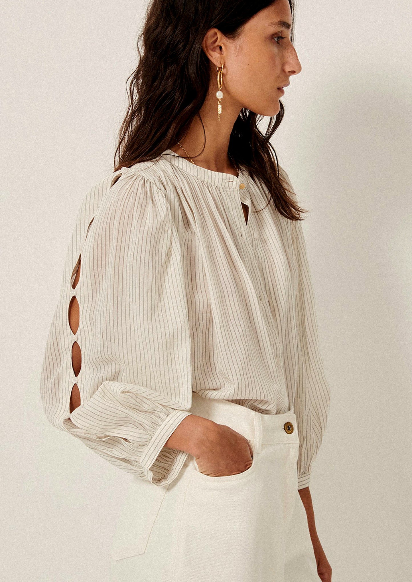 A woman wearing a white blouse with black pinstripe pattern, and cutout detailing on sleeves.
