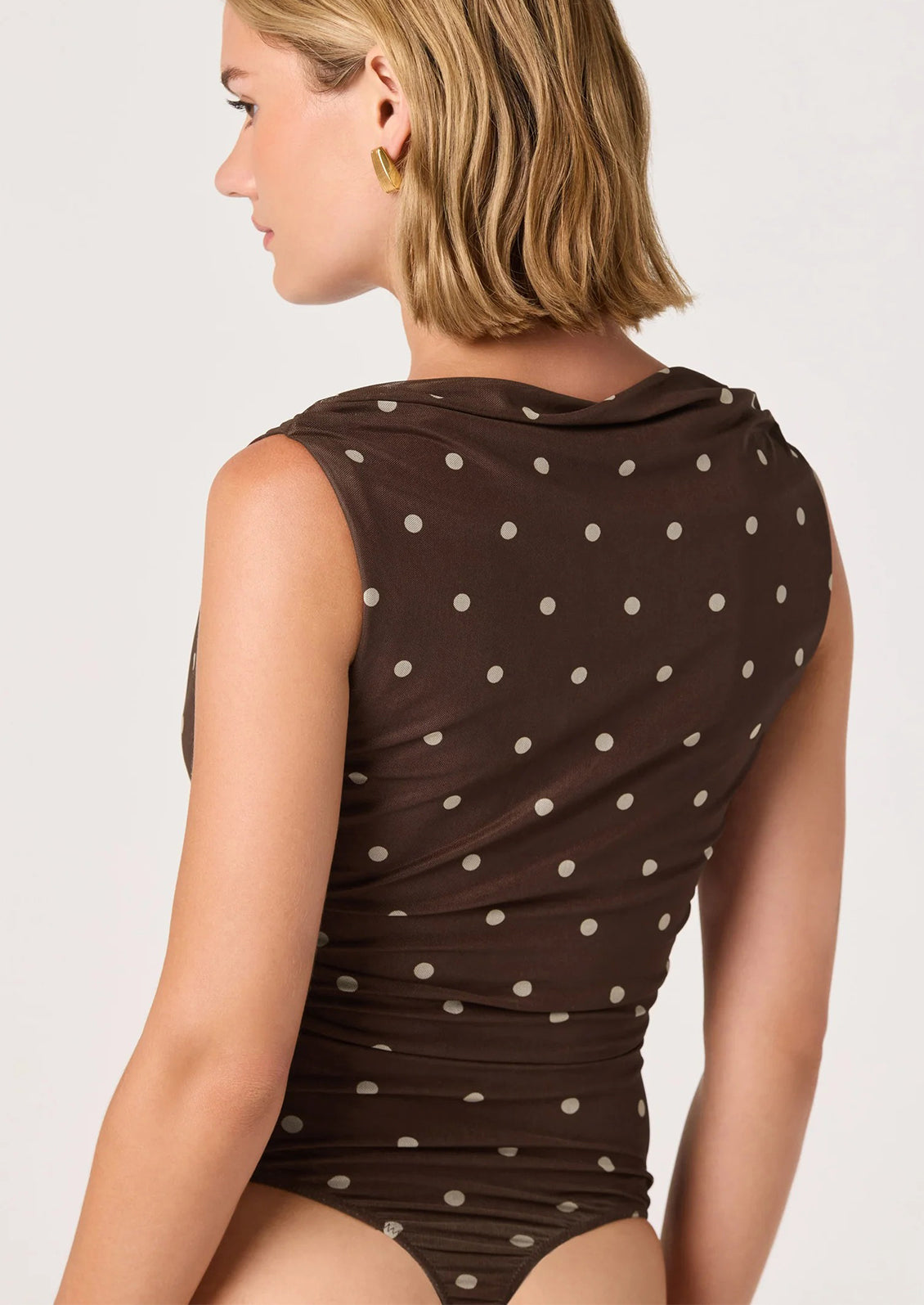 A person wearing a bodysuit in brown with cream polka dots.