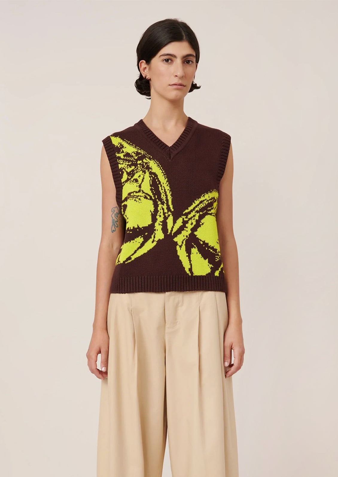 Person wearing a brown knit vest with a large yellow butterfly design.