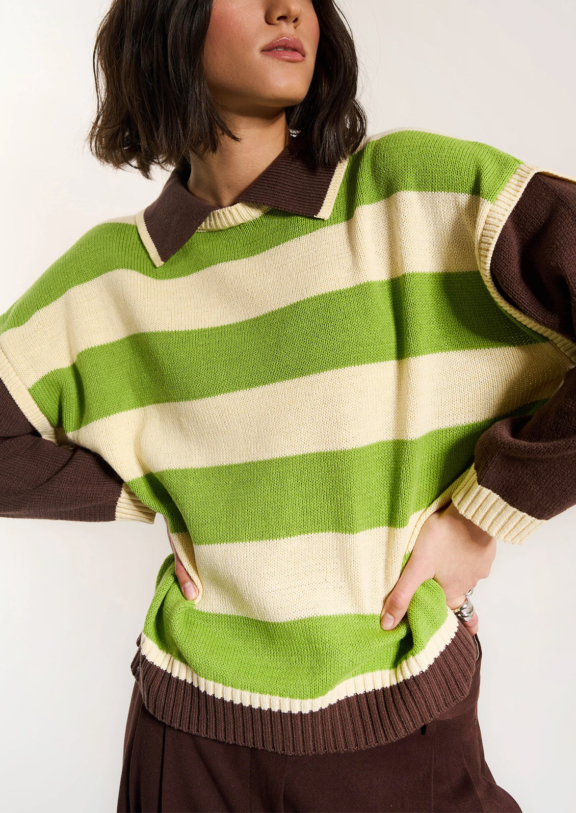 Person wearing a green and brown striped sweater with a plain background