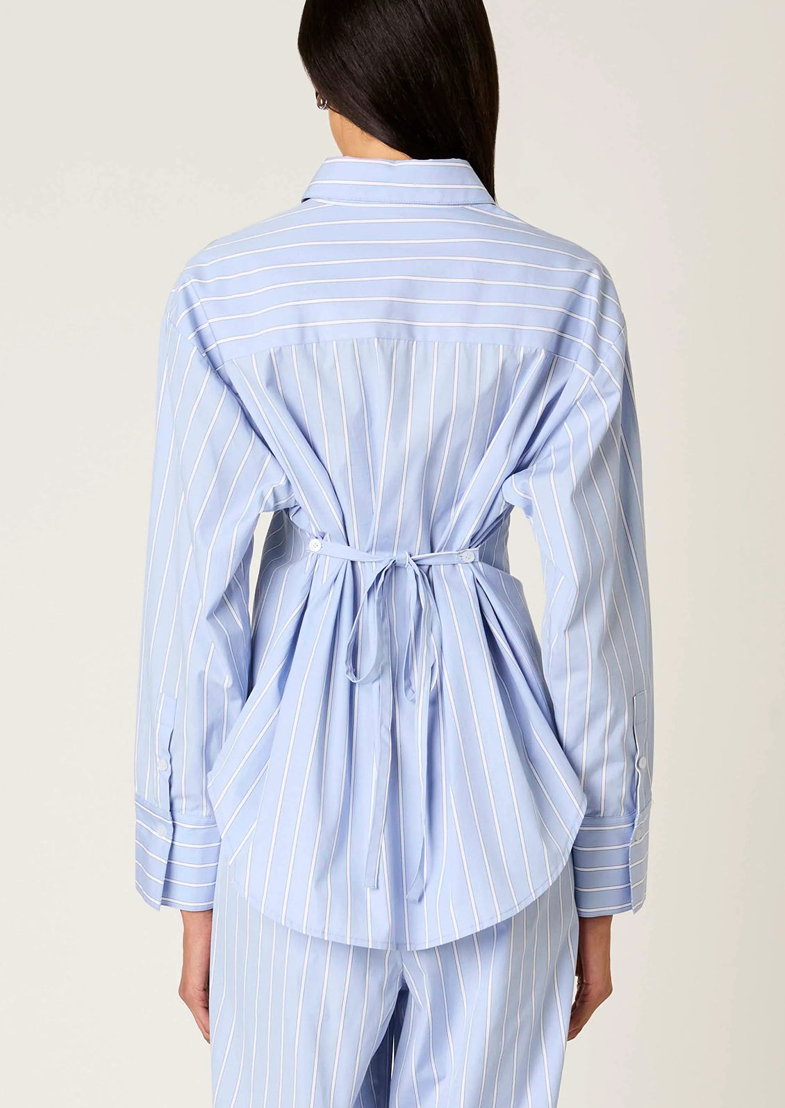 Person wearing a light blue striped shirt with a tie waist on a plain background