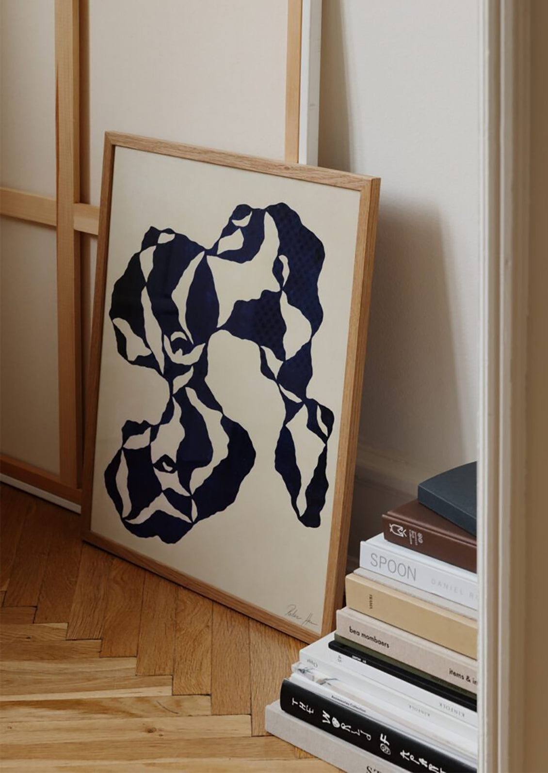 Framed abstract art leaning against a wall next to a stack of books.