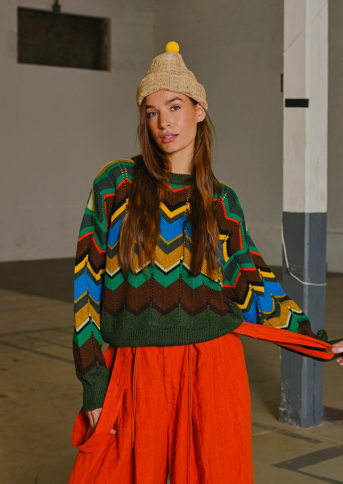 Woman wearing a colorful sweater and orange pants in an indoor setting