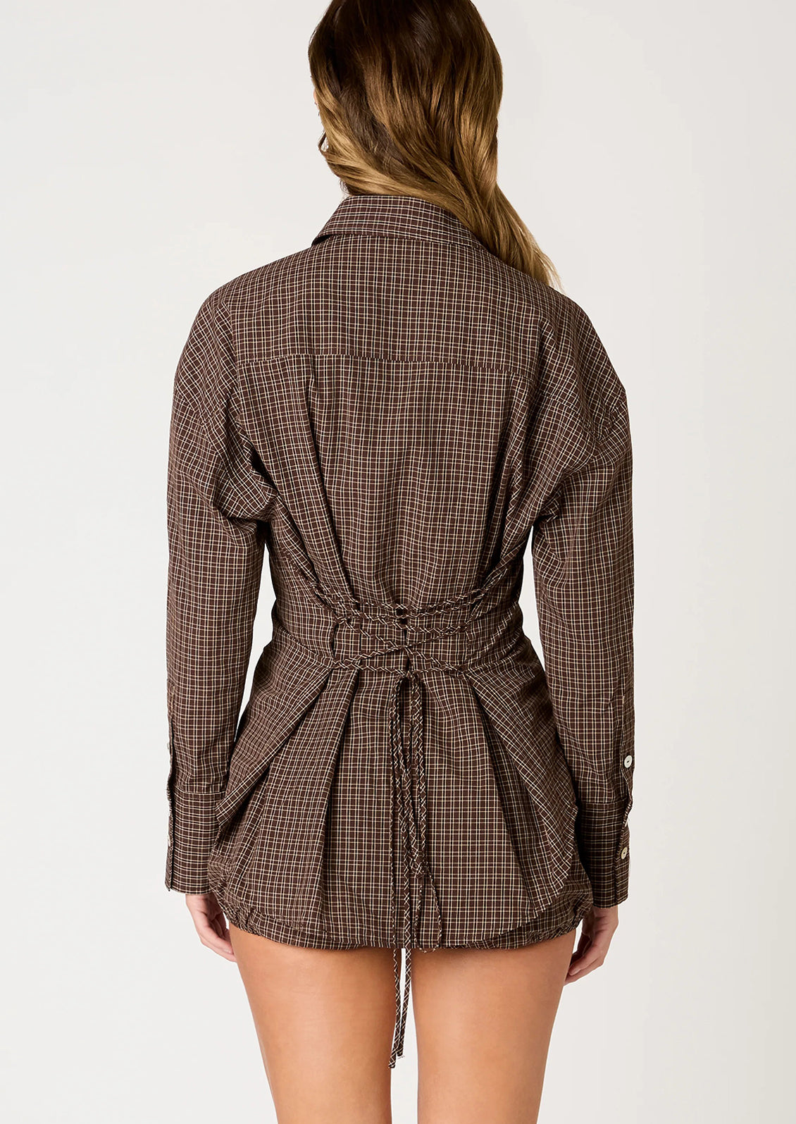 A person wearing a brown plaid button down shirt with lace-up back.