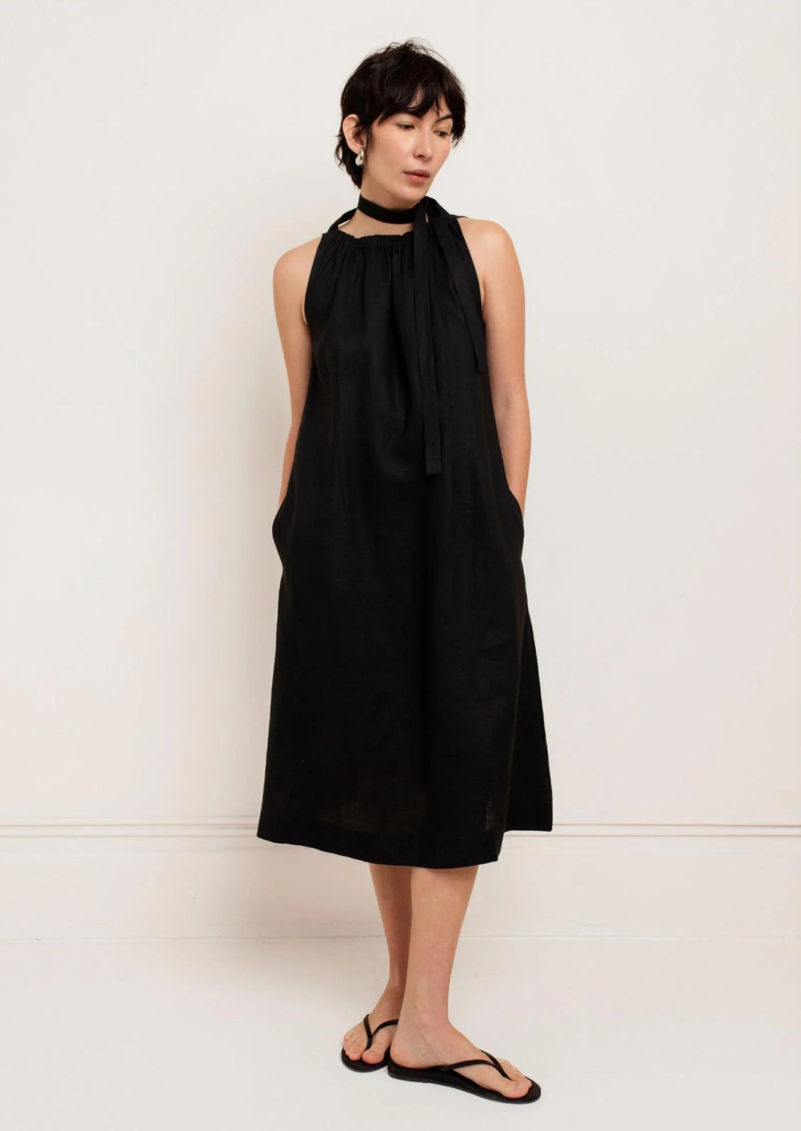 Woman wearing a black sleeveless dress with a scarf around her neck against a white background