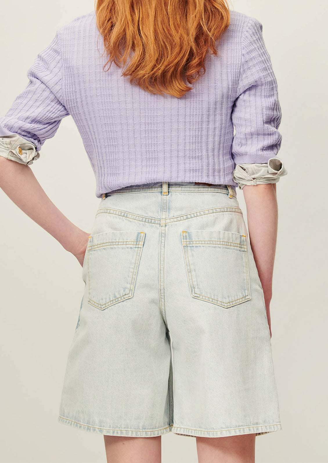 A person wearing a pair of denim bermuda shorts in light blue stonewash.