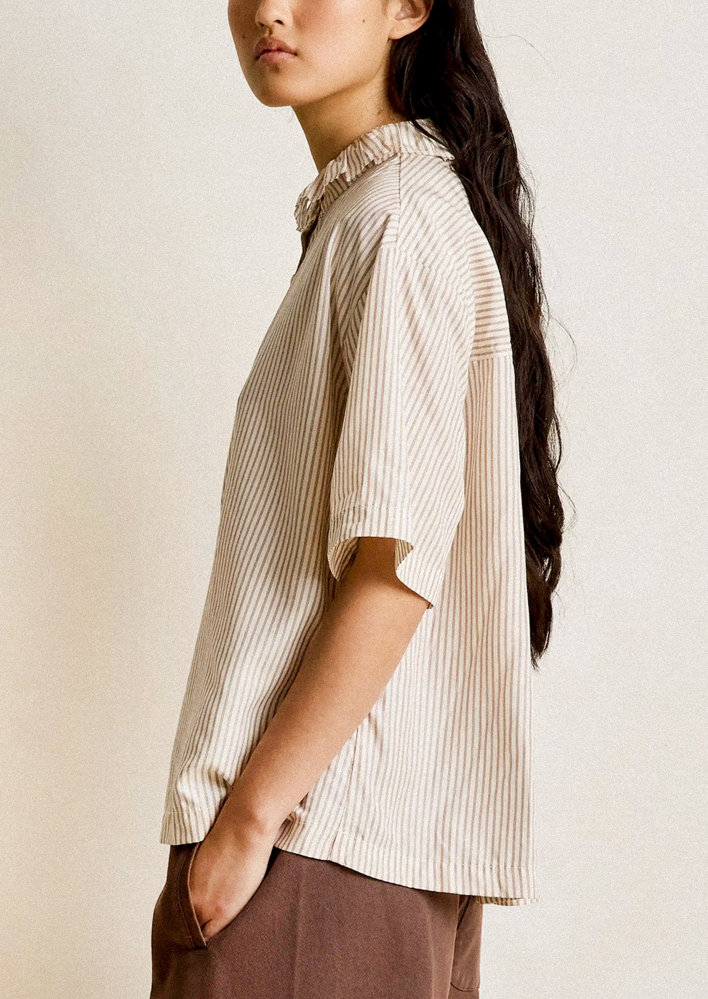Woman wearing a beige striped shirt against a plain background