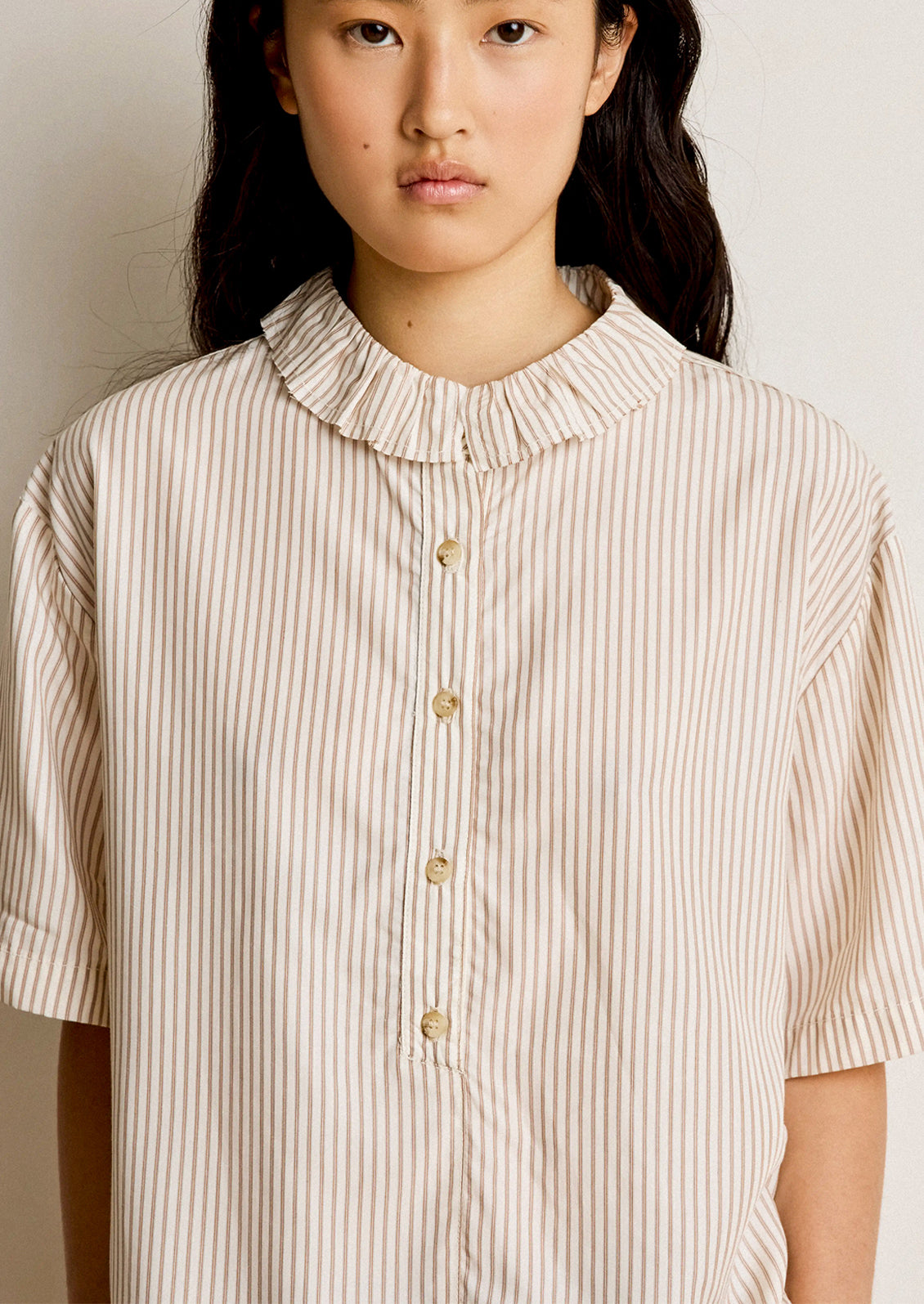 Woman wearing a beige and brown striped shirt with a high collar.
