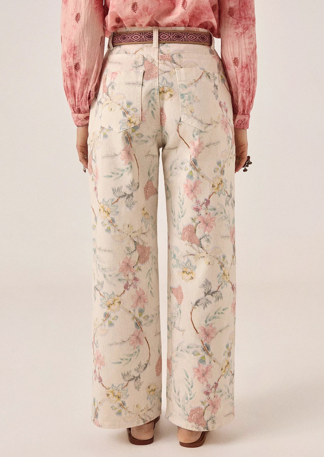A person wearing a pair of white denim pants with pastel floral print.