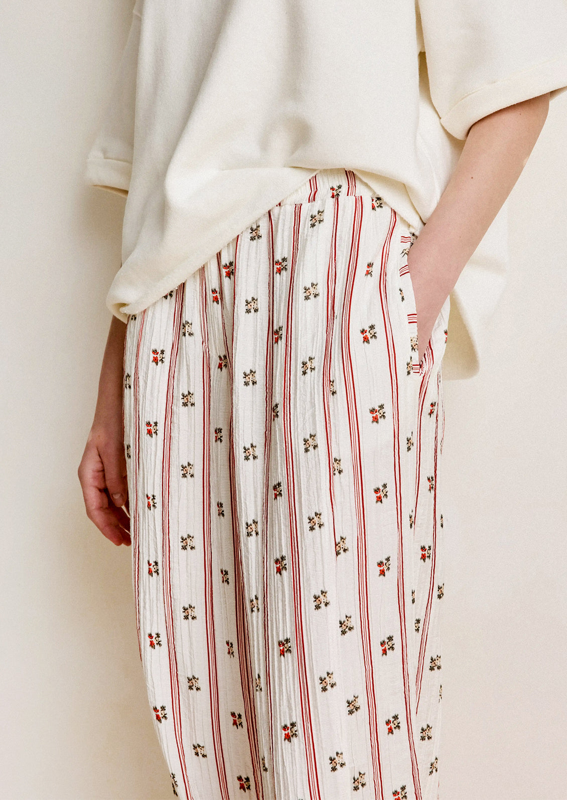 Person wearing a white top and patterned pants with red stripes and small floral designs.