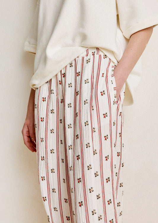 Person wearing a white top and patterned pants with red stripes and small floral designs.