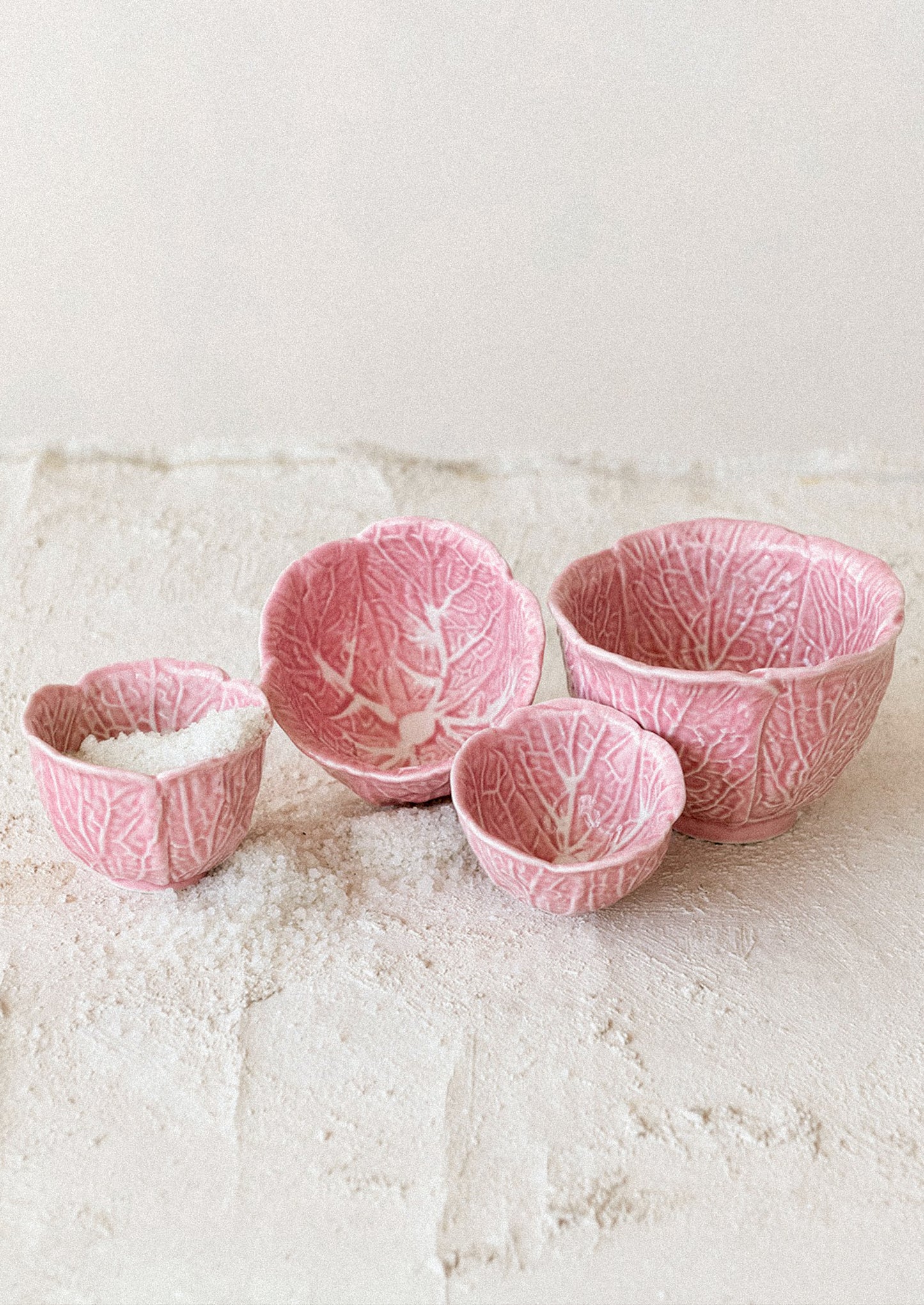 Set of four pink ceramic bowls with leaf pattern on a textured surface