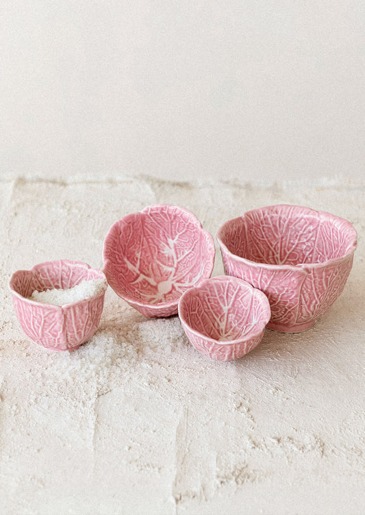 Set of four pink ceramic bowls with leaf pattern on a textured surface