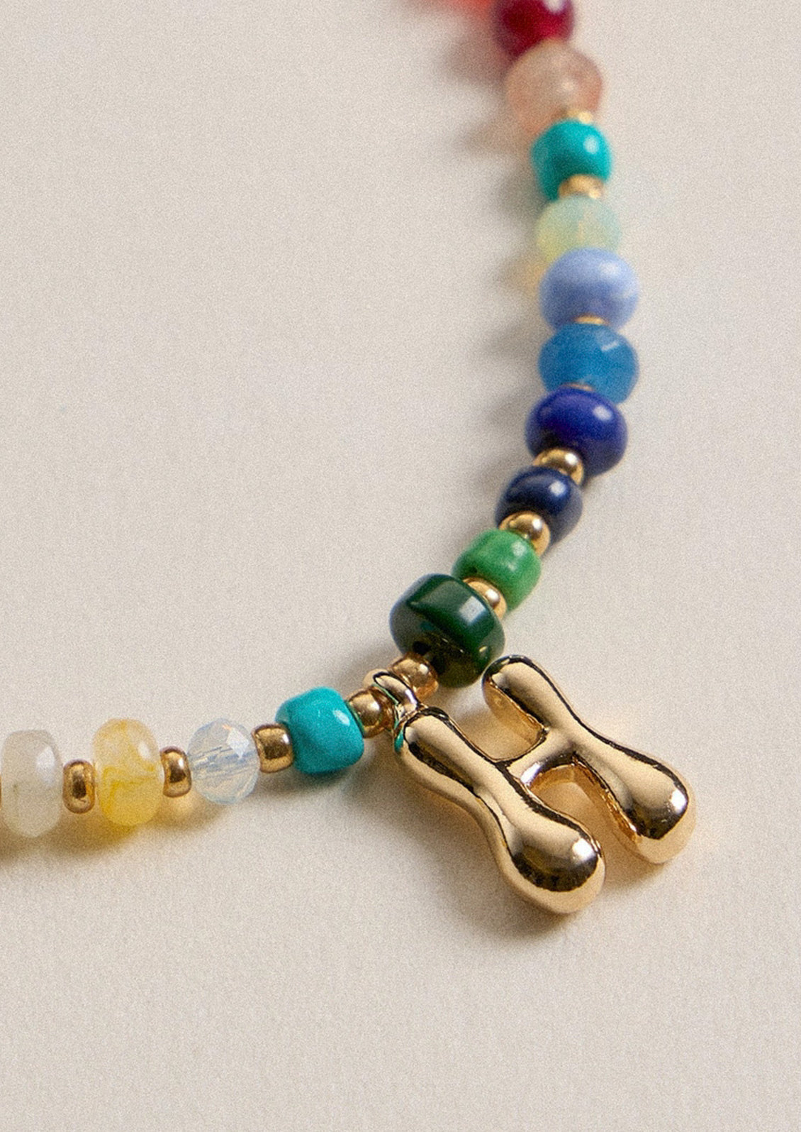 A colorful beaded necklace with a gold H charm.