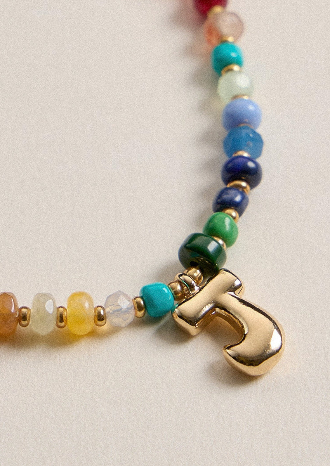 A colorful beaded necklace with a gold J charm.
