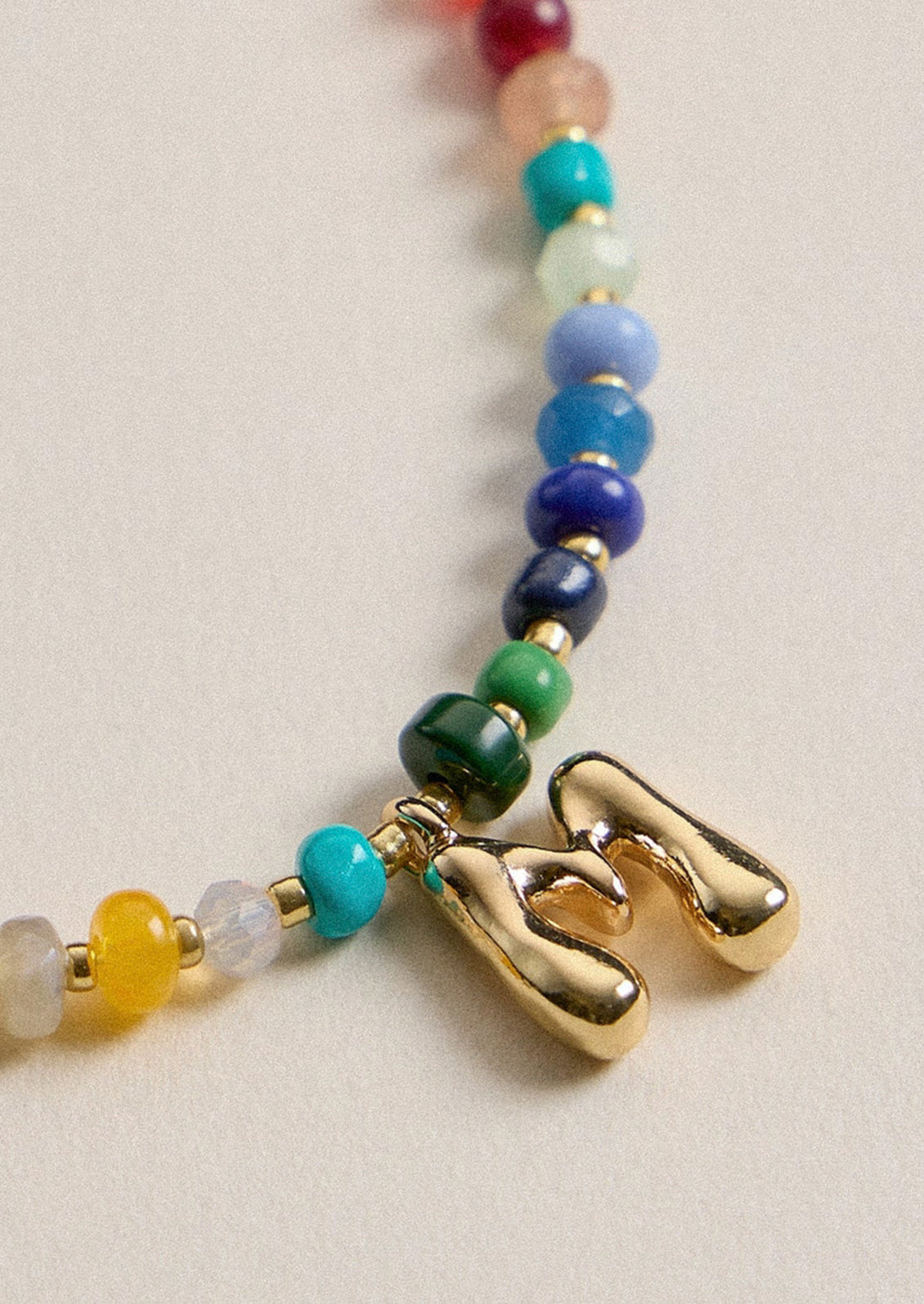 A colorful beaded necklace with a gold M charm.