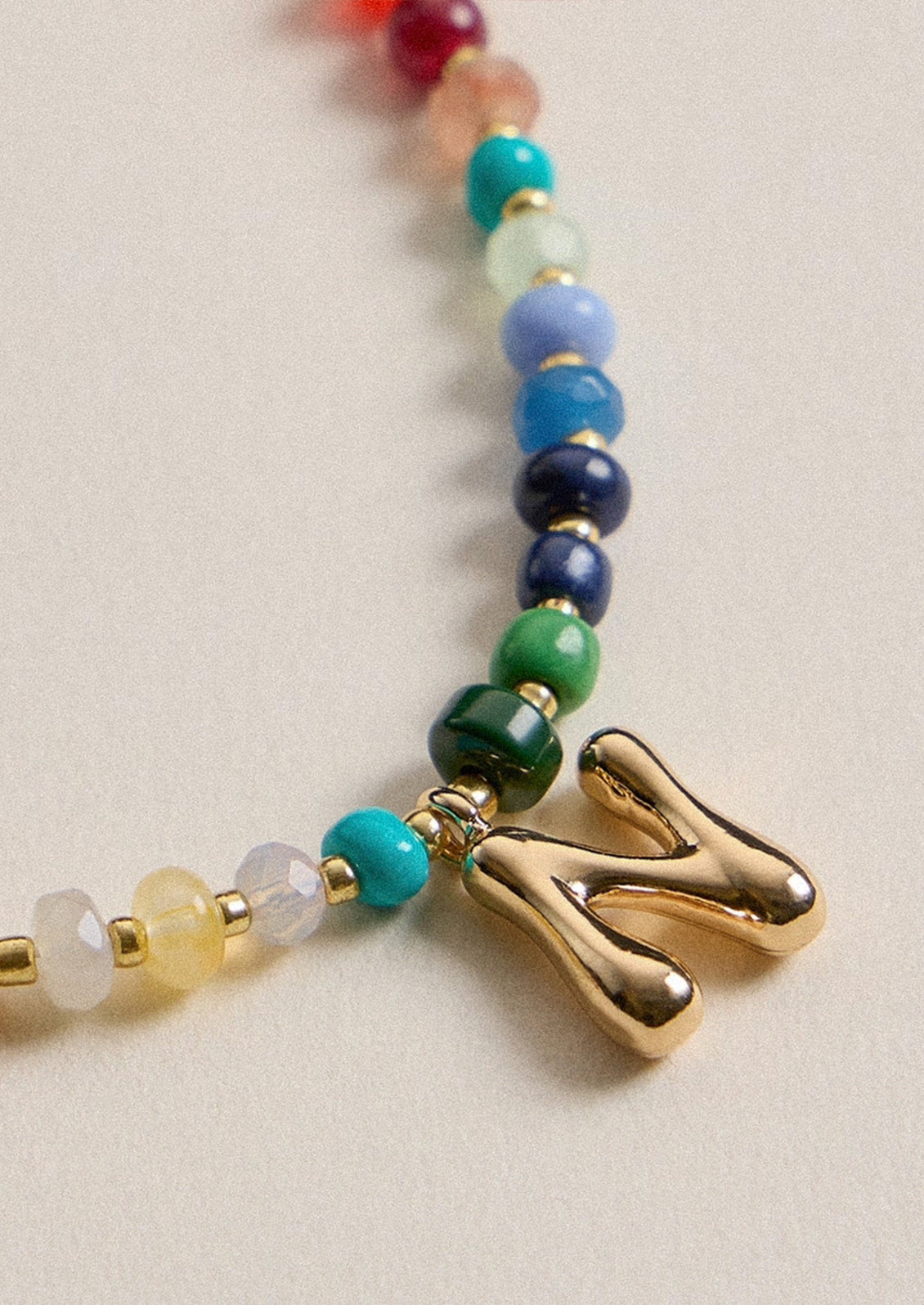 A colorful beaded necklace with a gold N charm.