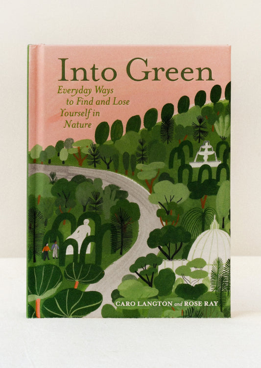 A hardcover copy of the book "Into Green" by Caro Langton and Rose Ray standing on a table. The cover features a green nature scene with a pink sky.
