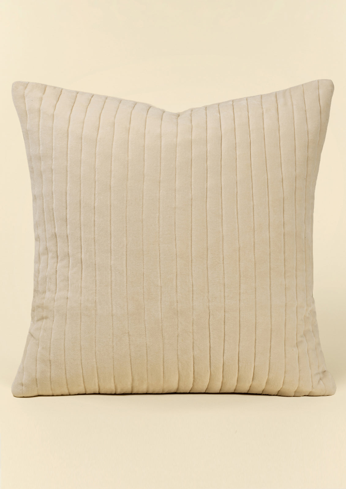 A square ivory velvet throw pillow with vertical ribbed quilting.